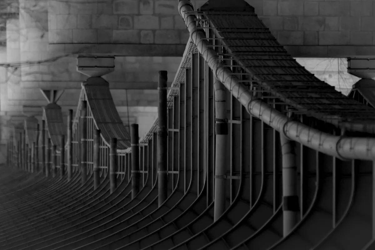 Monochrome sweep of bridge railings and cables curving into the distance